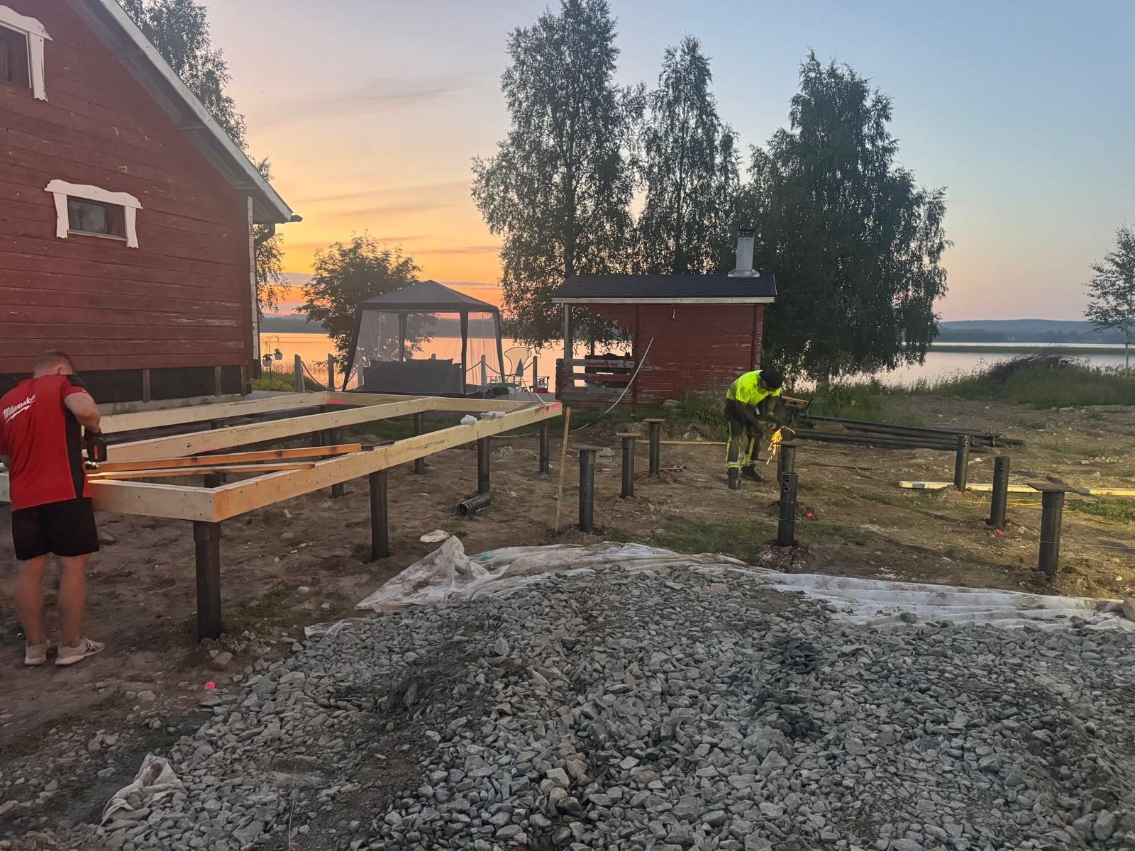 Arbetare bygger trästomme på skruvpålegrund vid sjö